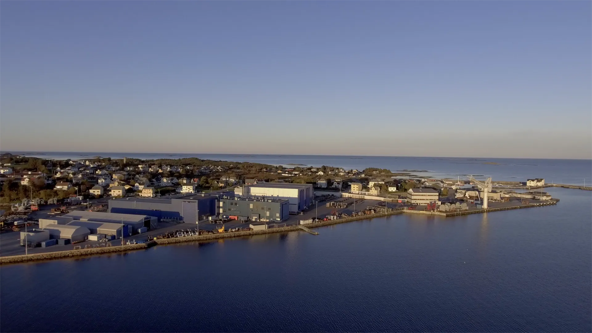Aerial view of an industrial yard with quay and crane on a headland, sea to the horizon.