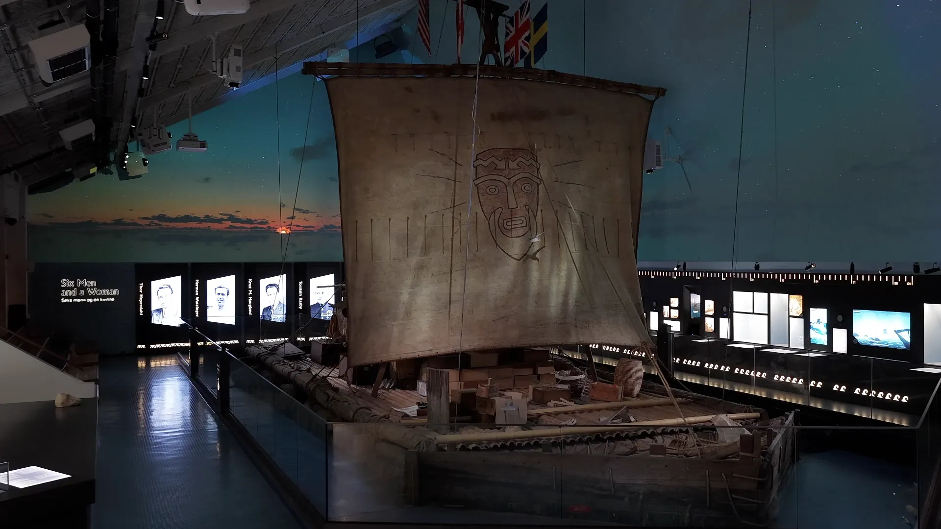 The Kon-Tiki raft with a sail decorated with a face, on display in the museum hall with portraits in the background.